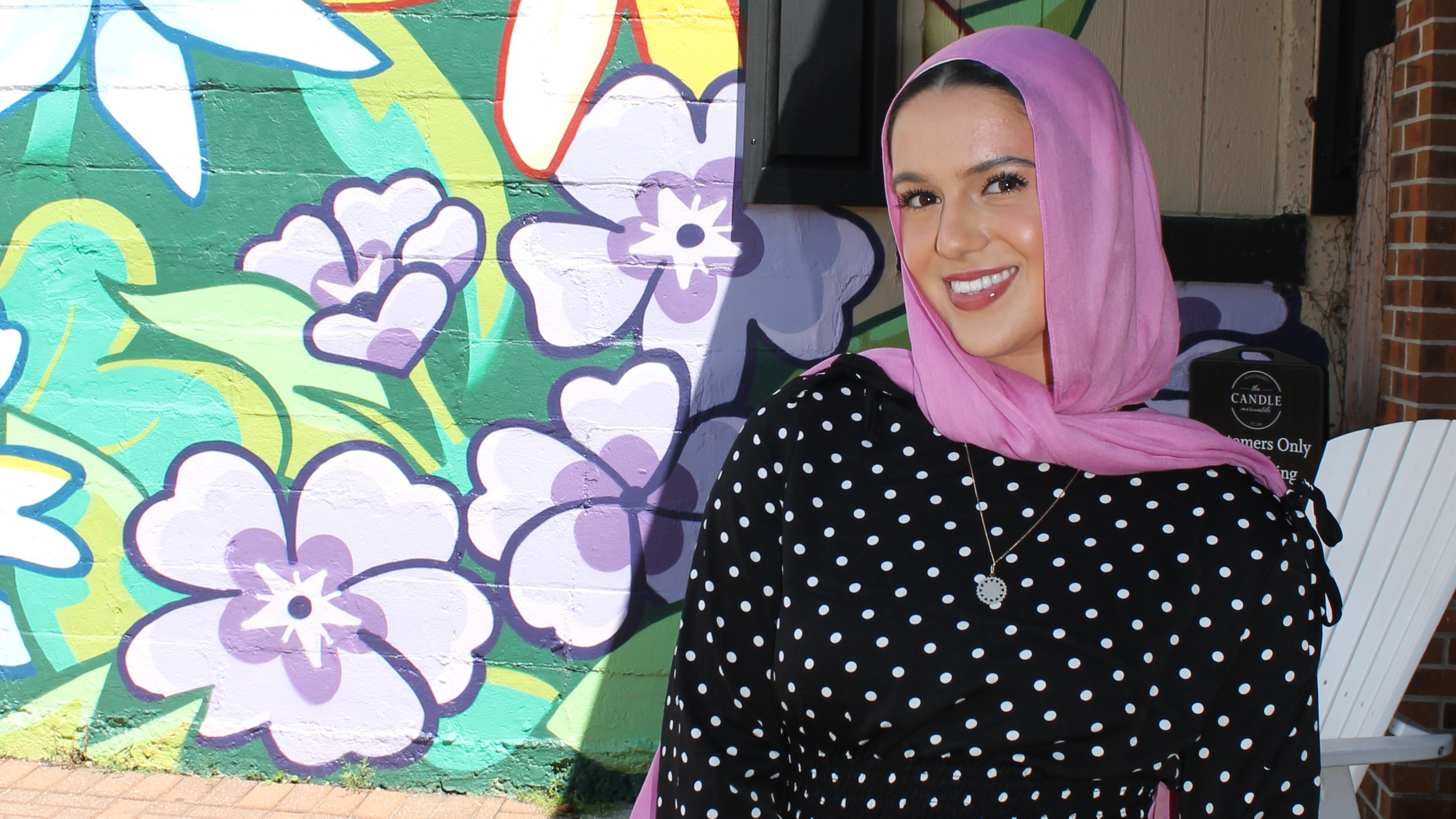 Yasmeen Kaloti smiles in front of a floral background while wearing a pink scarf headscarf and black shirt Yasmeen Kaloti smiles in front of a floral background while wearing a pink scarf headscarf and black shirt